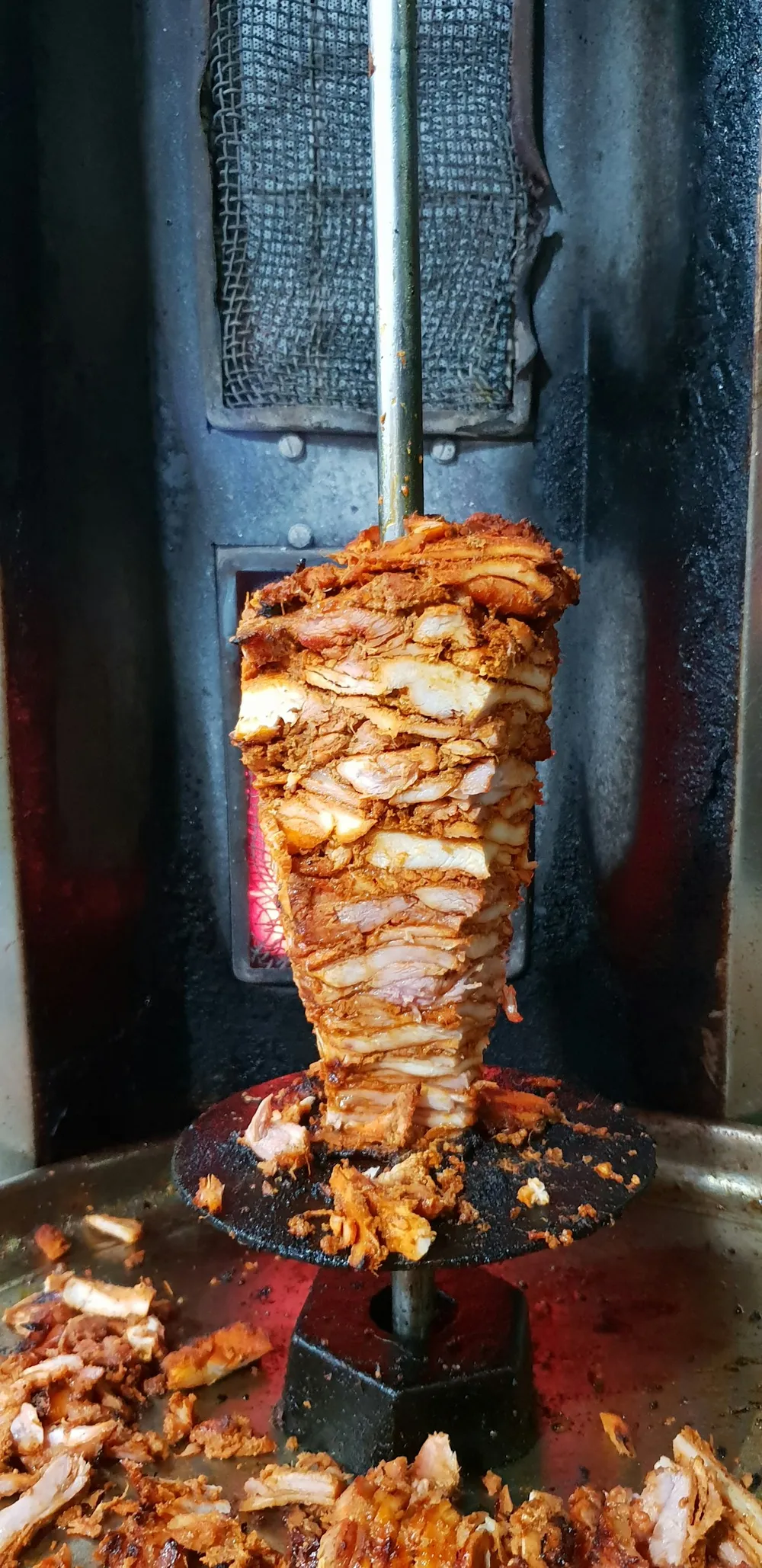 Halal doner meat stacked on a vertical rotisserie spit