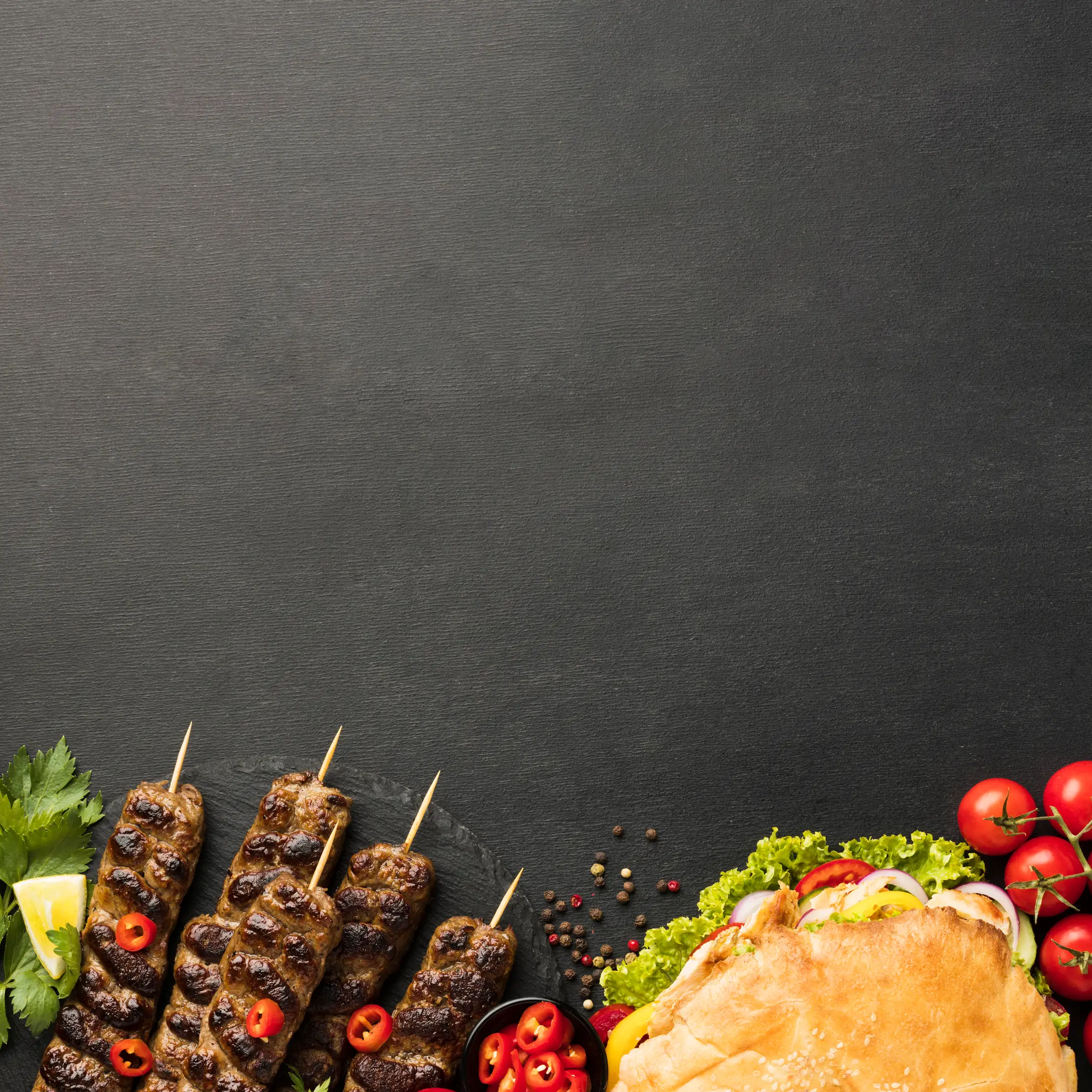 Grilled kofte skewers with chilli, lemon and parsley, and a loaded kebab wrap, laid out on dark slate